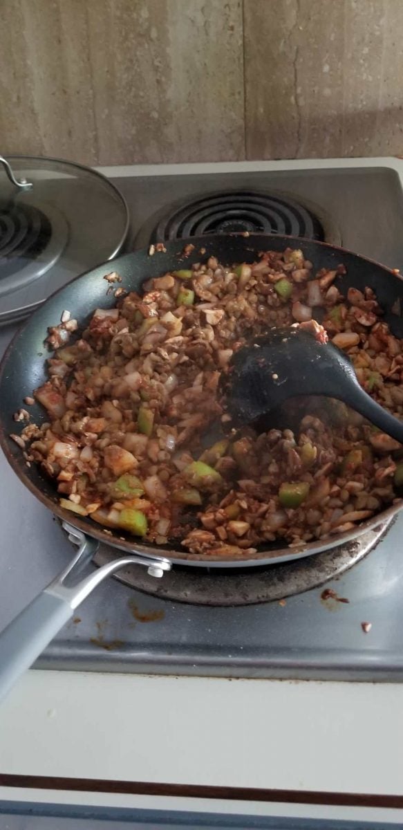 Stir in spices for vegan walnut wellington filling, including nutritional yeast, tomato sauce, minced garlic, poultry spice, flax seed, and black pepper